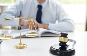 judge's gavel with scales of justice in front of a man reviewing law in a book